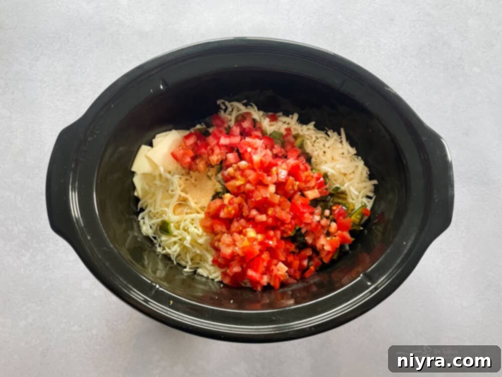 Shredded cheeses, roasted peppers, chopped tomatoes, cream, and garlic in a slow cooker, ready to be combined.