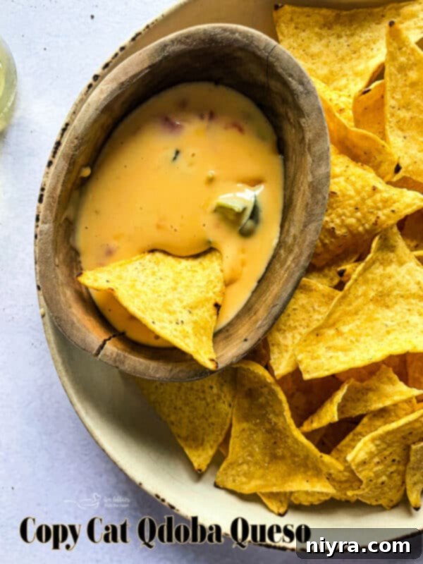 Hero shot of the Copycat Qdoba Queso in a bowl with chips and fresh lime
