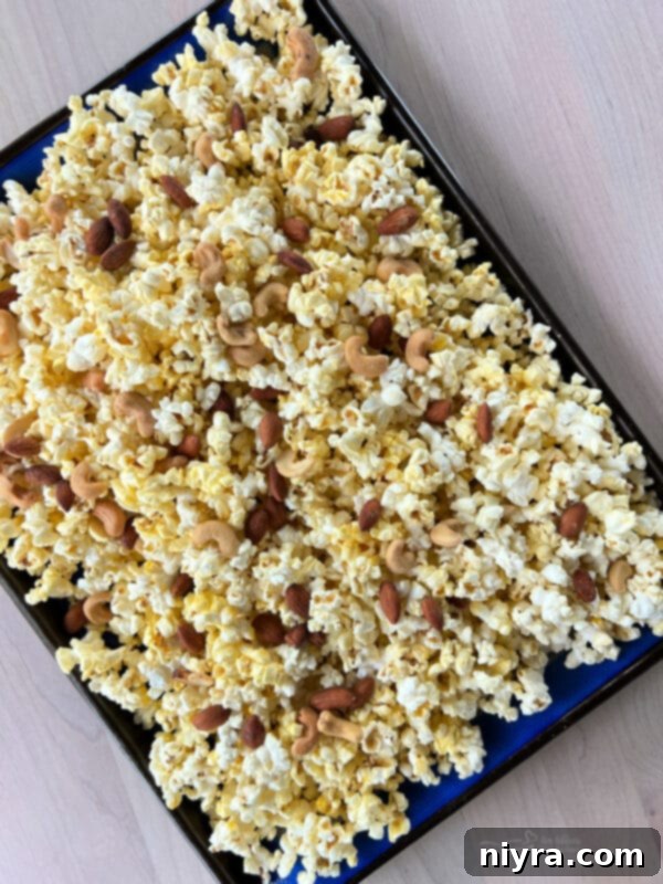 Ultimate Homemade Caramel Chocolate Nut Popcorn 11 Popped popcorn and mixed nuts spread evenly on a parchment-lined baking sheet