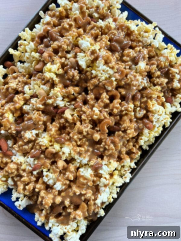 Ultimate Homemade Caramel Chocolate Nut Popcorn 15 Pouring the warm caramel mixture over popcorn and nuts on a baking sheet