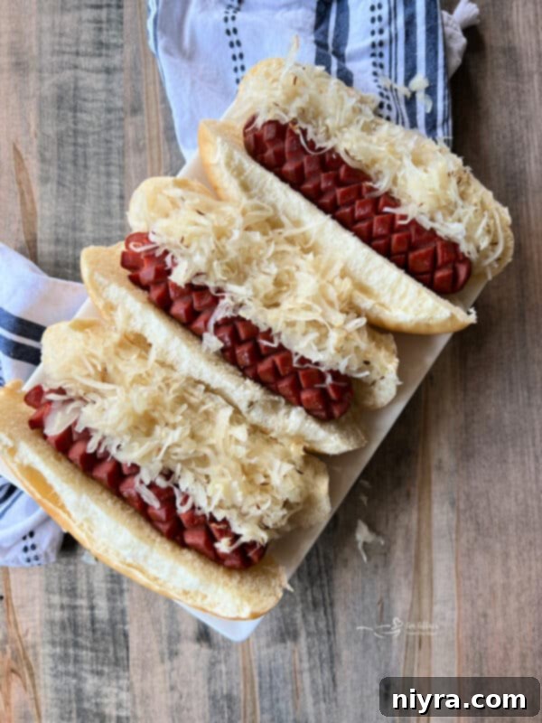 Smoky Dogs with Zesty Kraut 2 Smoked hot dogs and kraut in buns on a plate, garnished with caraway seeds