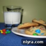 Side view of a few rainbow cookies on a white plate and a glass of milk on a table