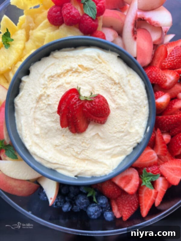 A beautifully arranged fruit platter featuring grapes, strawberries, blueberries, and melon, with a bowl of creamy vanilla almond fruit dip at the center.