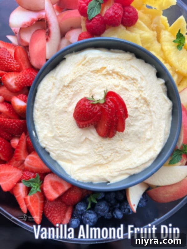 A tantalizing close-up of the creamy vanilla almond fruit dip, perfectly swirled in a bowl, with a variety of fresh fruits like strawberries, blueberries, and grapes artfully arranged around it.