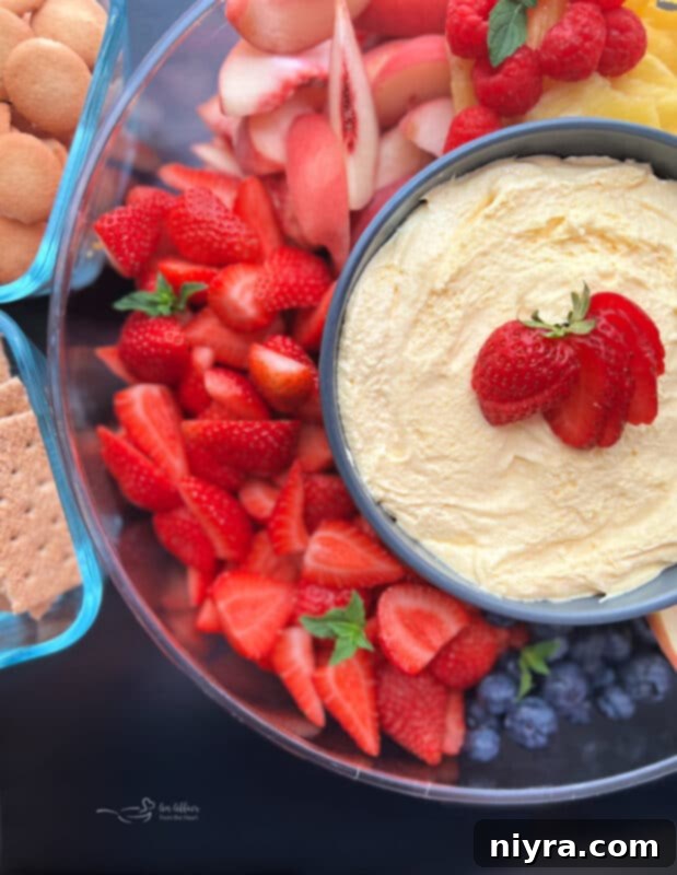 A close-up of fresh strawberries, blueberries, and apple slices artfully arranged around a bowl of vanilla almond fruit dip, ready for dipping.