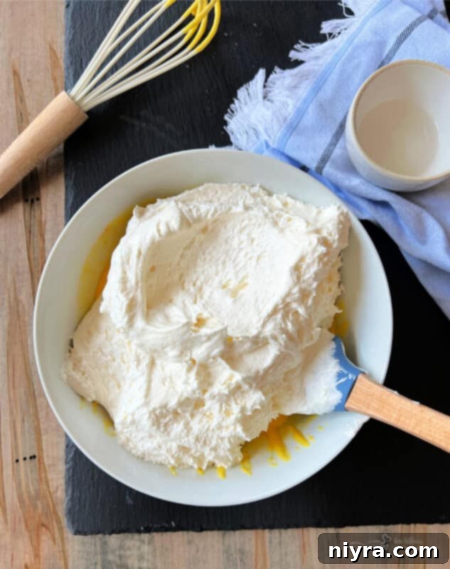 A spatula gently folding soft, whipped Cool Whip into the vanilla pudding and milk mixture in a bowl, creating a light and airy consistency.