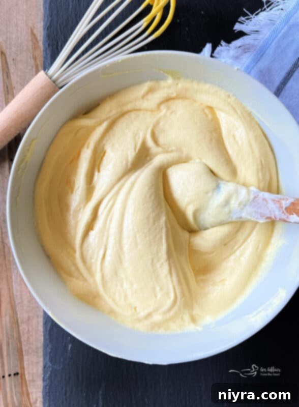 Pure almond extract being drizzled into the creamy fruit dip mixture in a bowl, with a spoon nearby for tasting and adjusting flavor.