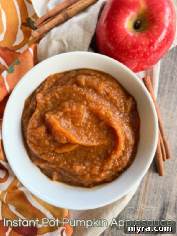 A bowl of Instant Pot Pumpkin Applesauce with fresh apples in the background