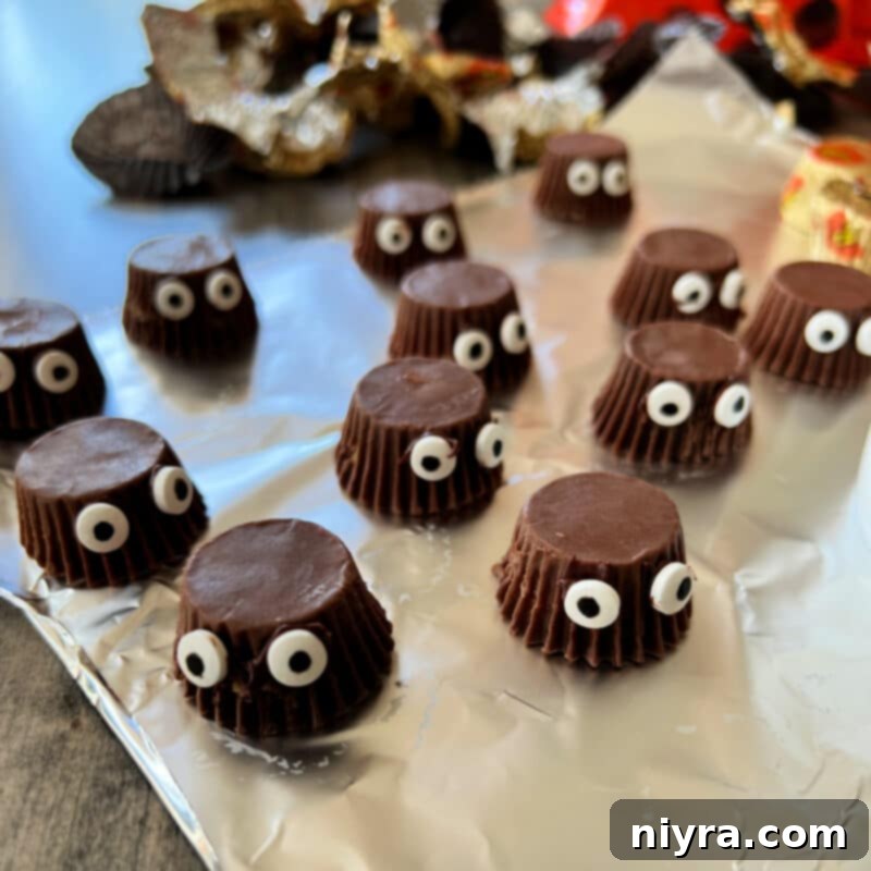 Close-up showing candy eyeballs being attached to miniature Reese's Peanut Butter Cups with melted chocolate.