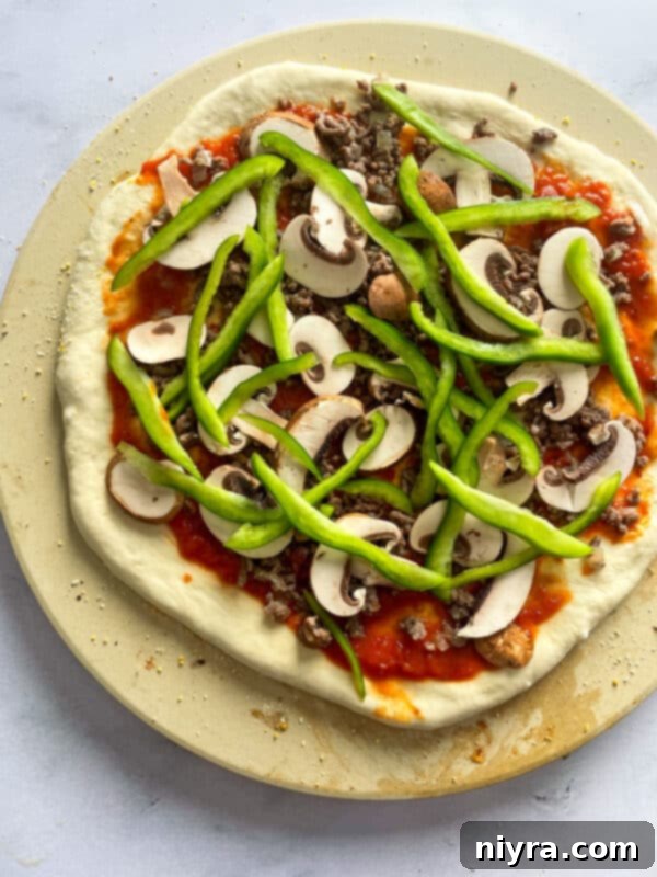 Adding mushrooms, peppers, olives, and pepperoni to a pizza.