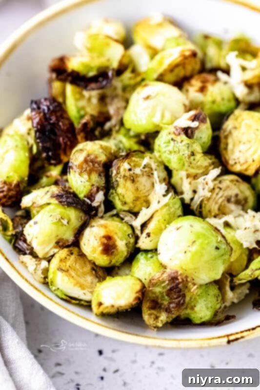 A close-up shot of perfectly roasted Brussels sprouts in an air fryer basket, sprinkled with parmesan cheese.