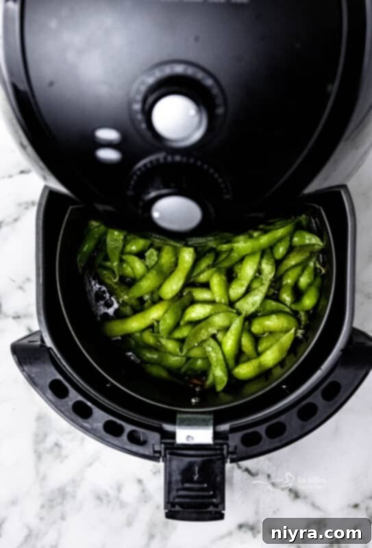 A vibrant green bowl of Air Fryer Edamame Beans, perfectly cooked and lightly seasoned, set against a dark background.