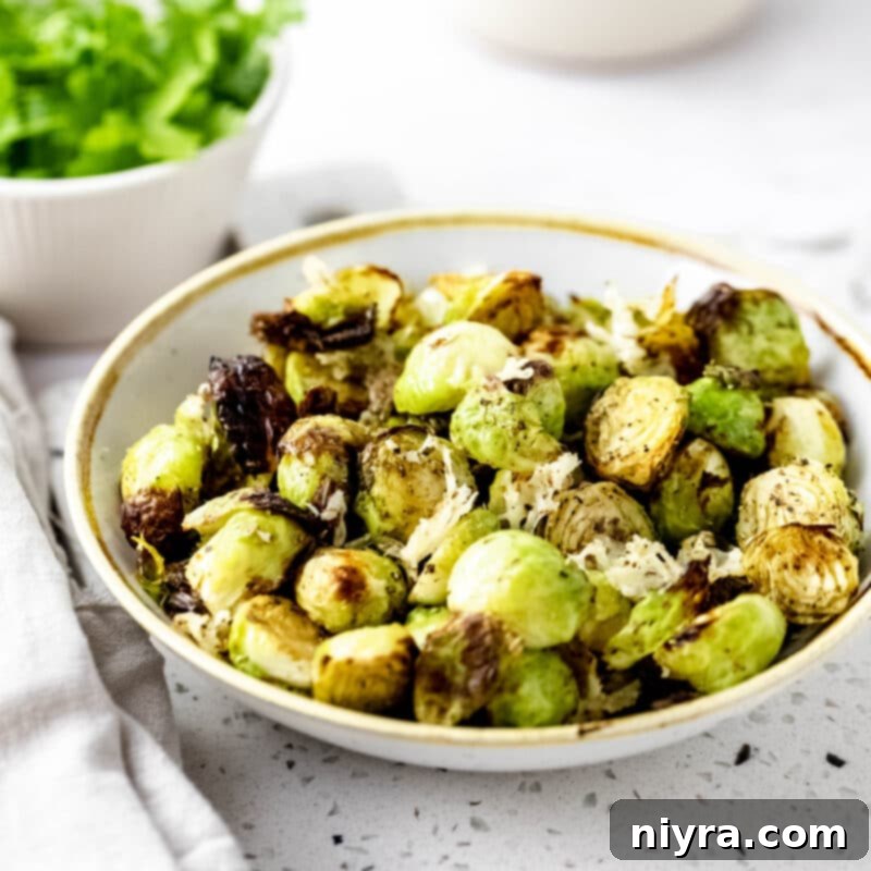 A bowl of seasoned Brussels sprouts, next to an air fryer and a container of shredded parmesan cheese.