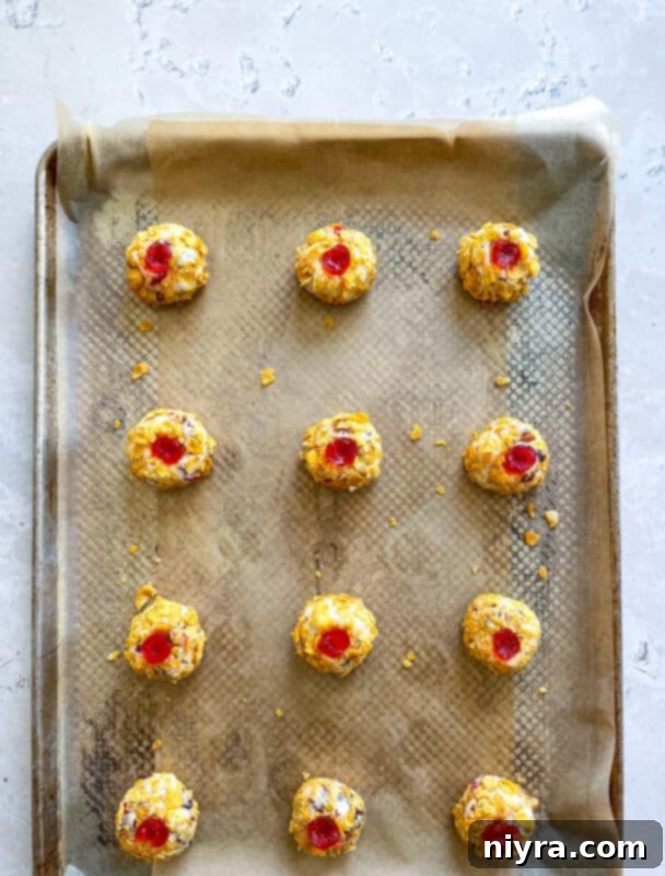 Maraschino cherry quarters being pressed into the top of each cookie dough ball.