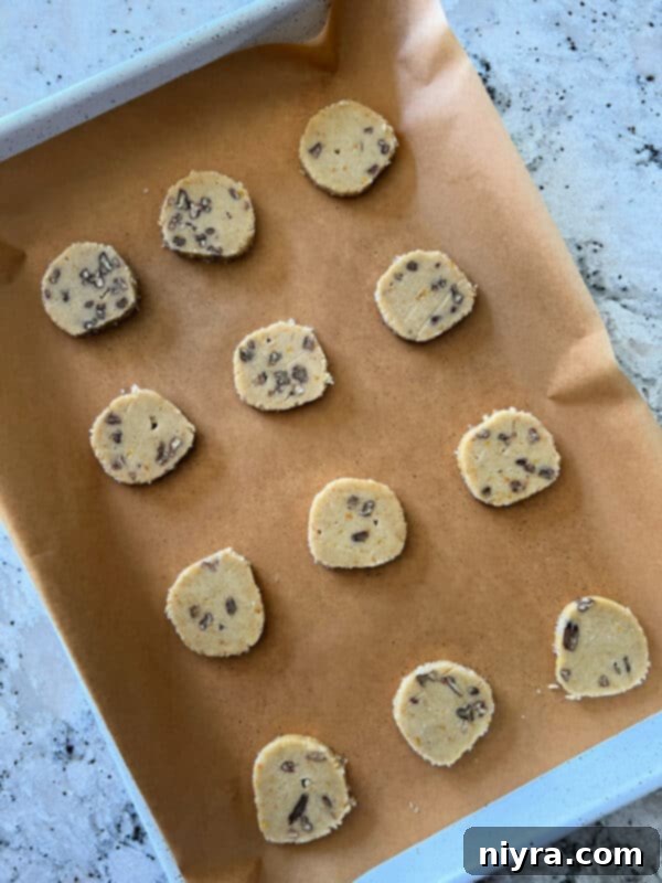 Cookie dough log being rolled in decorator sugar crystals on plastic wrap.