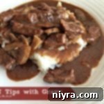 Beef Tips with Gravy over mashed potatoes on a white plate