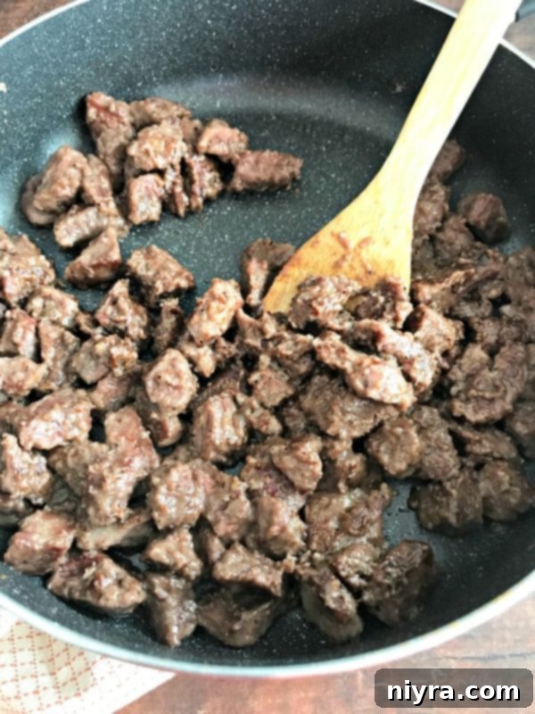 Beef tips coated in flour and spices, browning in a skillet to lock in flavor.