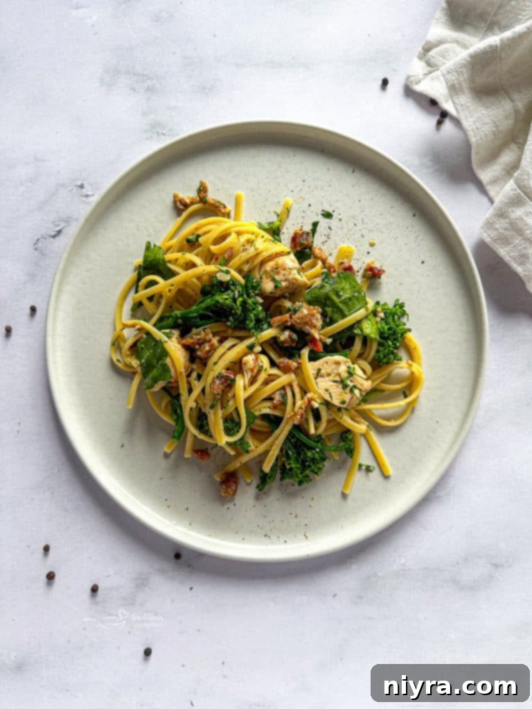 Close-up of a serving of Chicken Carbonara with a fork, showing the creamy sauce coating the pasta, chicken, and greens.