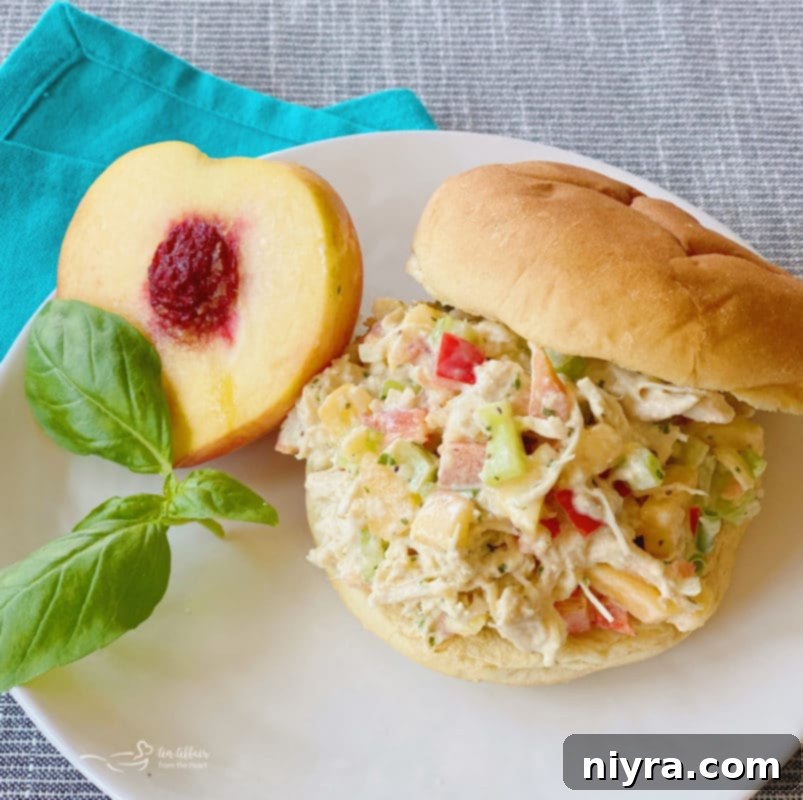 Peach Basil Chicken Salad sandwich on a white plate with fresh peach slices.