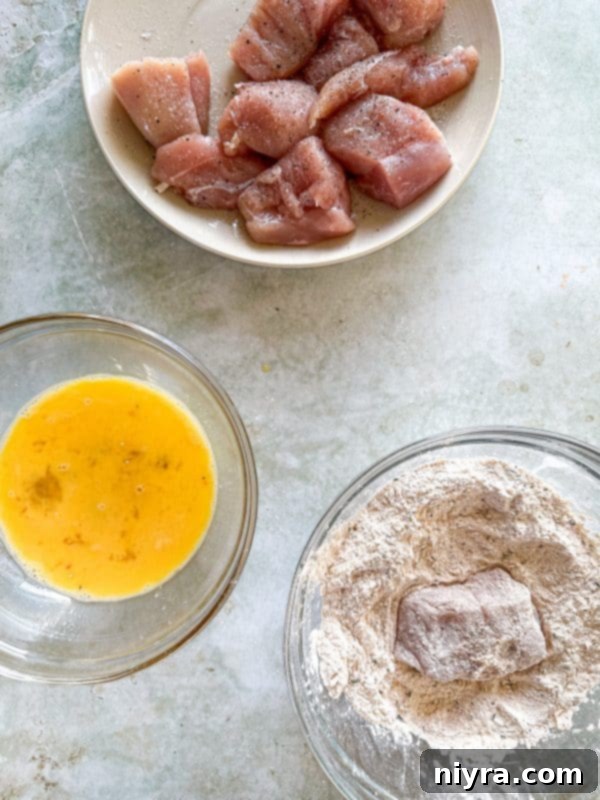 Chicken pieces being dredged in the seasoned flour mixture for the first coating layer.
