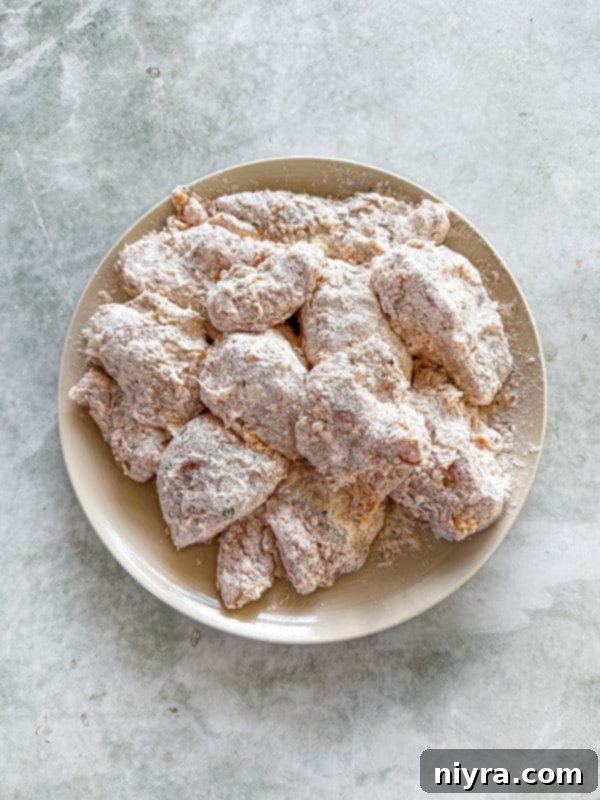 Double-dredged chicken pieces being carefully placed into hot oil in a skillet for frying.