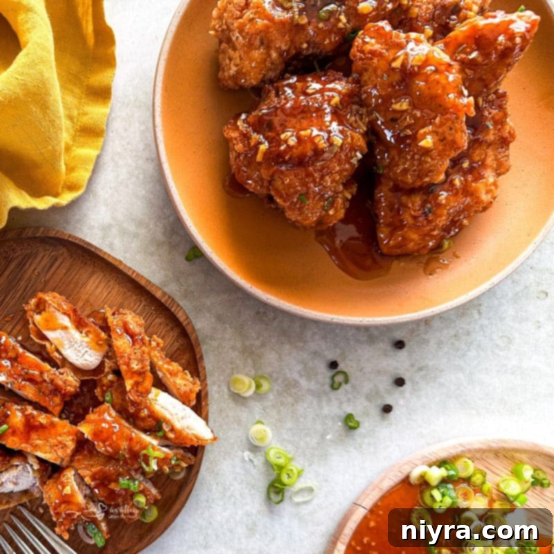 Serving platter with perfectly cooked honey fried chicken, garnished with fresh green onions and a bowl of dipping sauce.