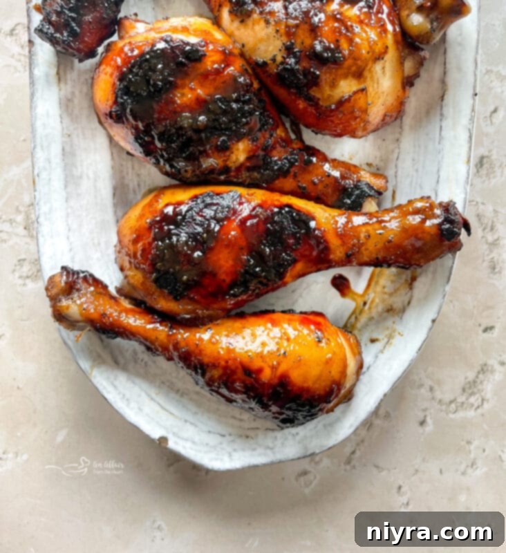 Grilled chicken legs coated in an Asian-inspired BBQ sauce, garnished with sesame seeds and green onions.