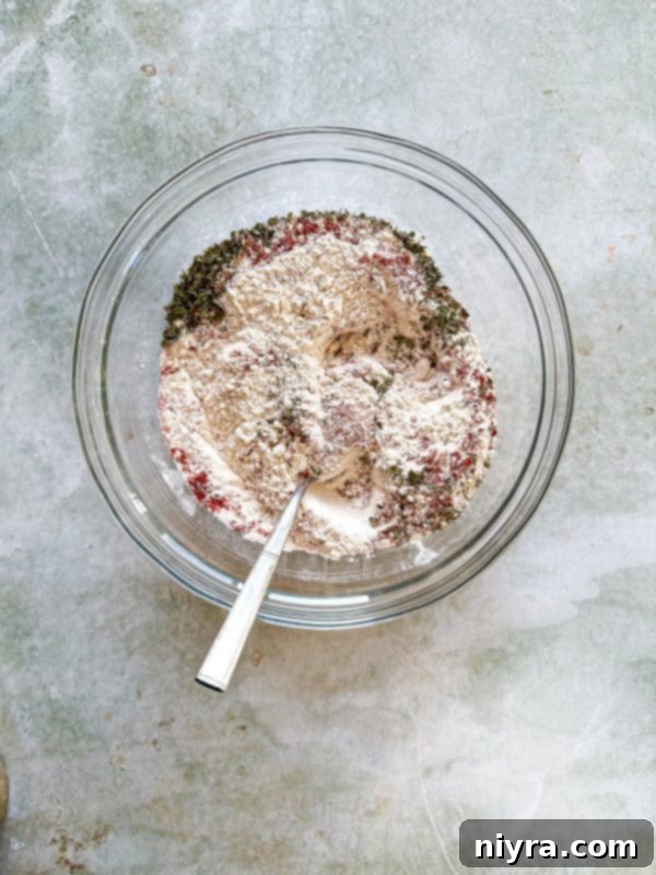 Dry ingredients - flour, oregano, paprika, and cayenne pepper - being combined in a large bowl.