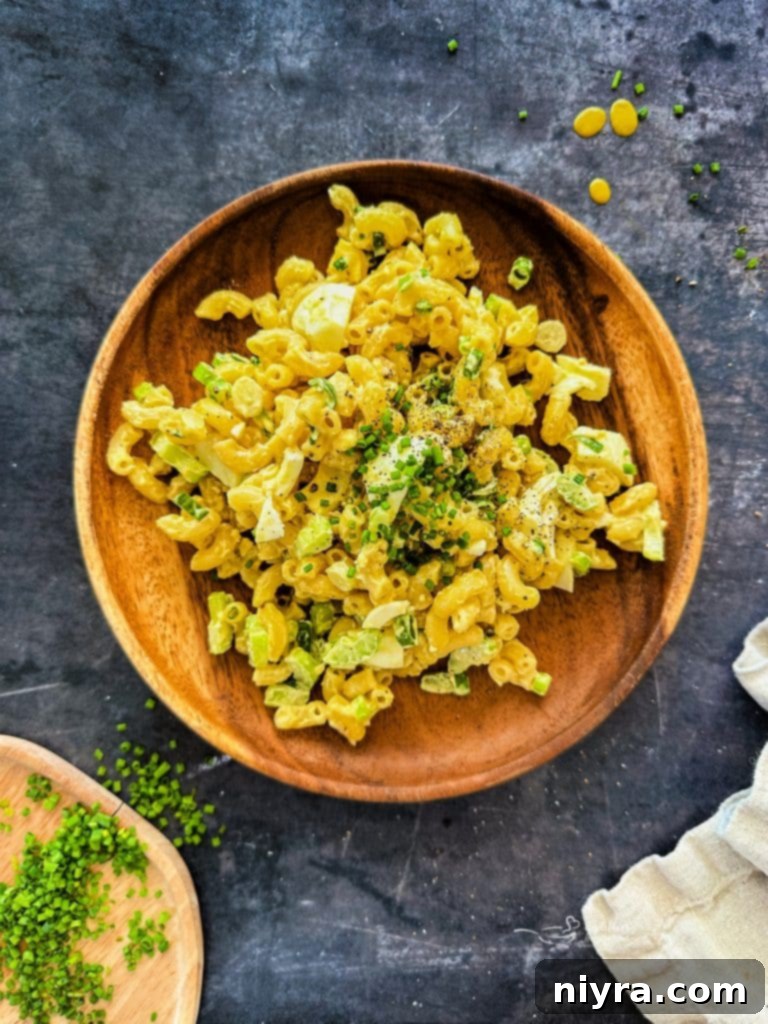A bowl of creamy Mom's Macaroni Salad, garnished with fresh chives, ready to be served at a family gathering.