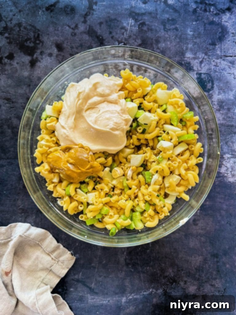 A large bowl containing cooked macaroni, chopped celery, and green onions, ready for the dressing.