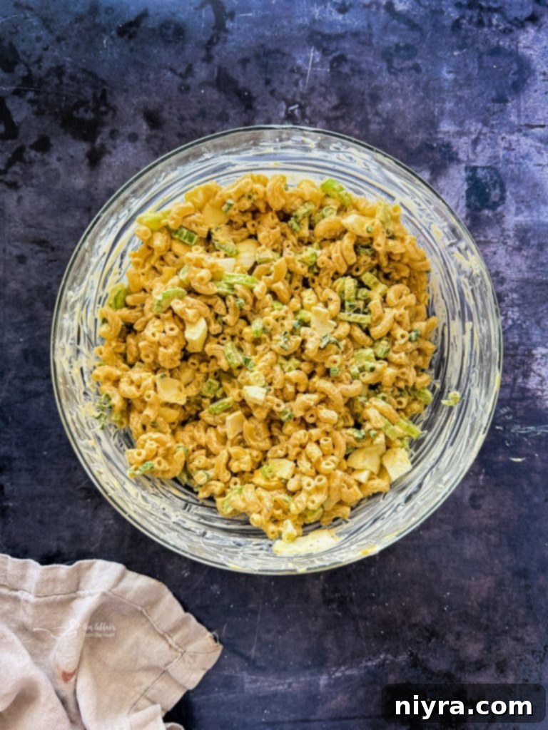 Mayonnaise and mustard being stirred into a bowl of macaroni and vegetables, forming the creamy dressing.