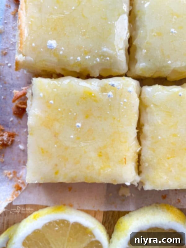 Four perfectly glazed lemon brownies with fresh lemons on a rustic surface