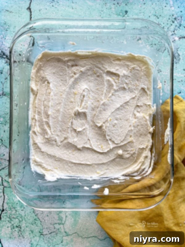 Lemon brownie batter evenly spread in a parchment-lined 8x8 baking dish, ready for the oven
