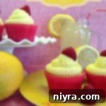 Side view Lemonade cupcakes on a yellow plate and on a white cake platter with half of lemons and a glass of lemonade on a pink surface. text "lemonade cupcakes with raspberry filling"