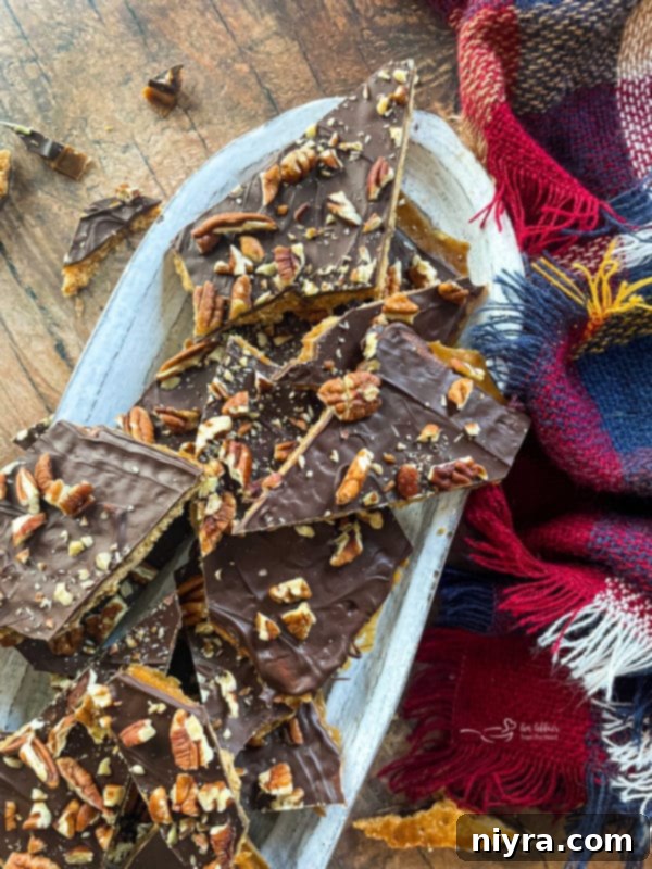 Delicious graham cracker toffee pieces adorned with pecans on a white oval plate, ready to be enjoyed.