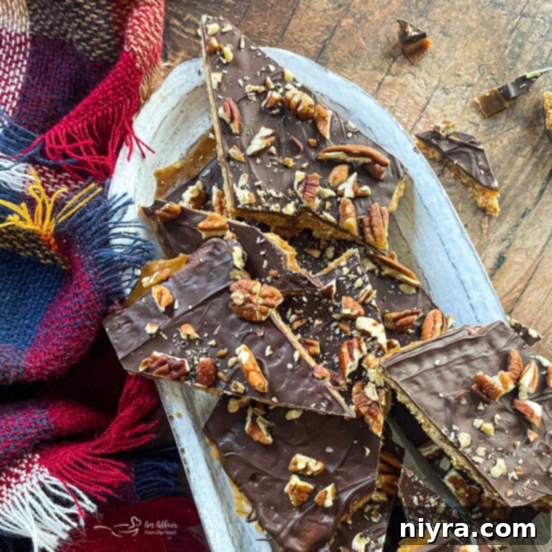 Assorted broken pieces of toffee bark with pecans and chocolate on a white oval dish, perfectly arranged.