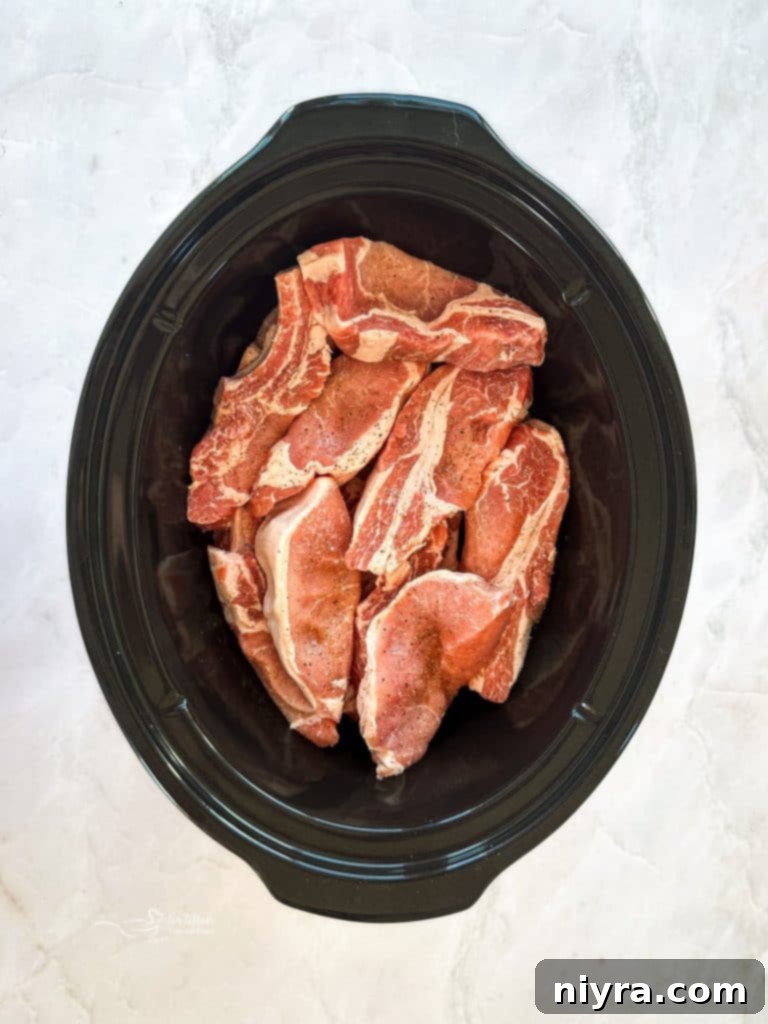 Raw country style pork ribs placed in the bottom of a slow cooker.