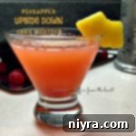 A close-up of a Pineapple Upside Down Cake Martini in a martini glass, garnished with a fresh pineapple wedge and a bright red maraschino cherry, ready to be enjoyed. The visual presentation evokes the classic dessert with a sophisticated twist.