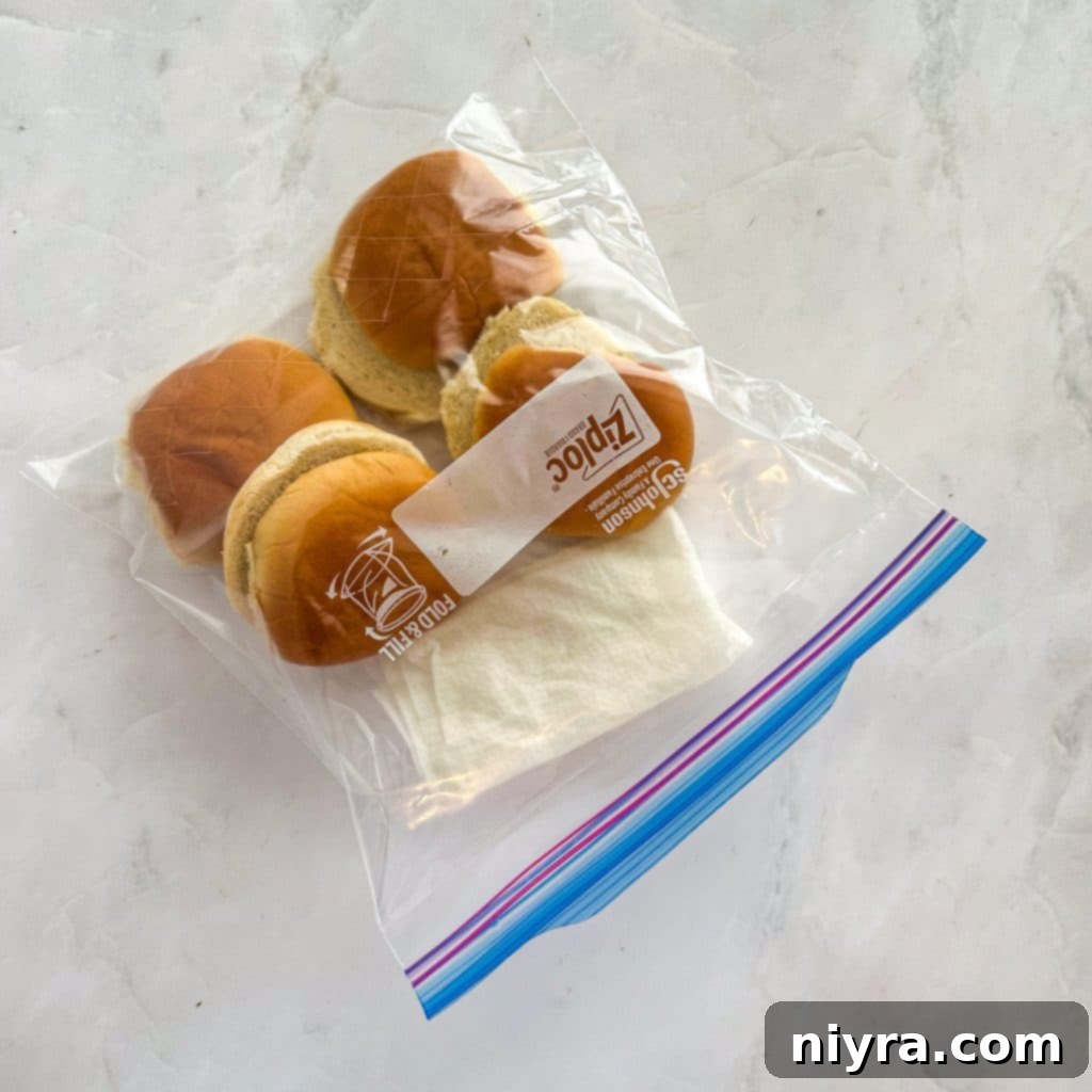 Hamburger buns being steamed in a microwave with a damp paper towel in a plastic bag.