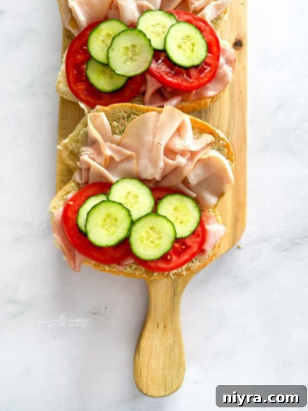 Adding slices of fresh cucumber and tomato to the hoagie.