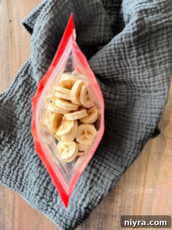 Sliced bananas arranged in a single layer on parchment paper for flash freezing.