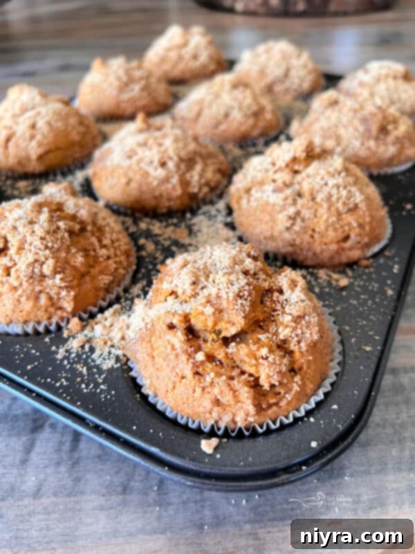 Close-up shot of golden brown Pumpkin Spice Banana Muffins baked in a muffin tin, topped with streusel.