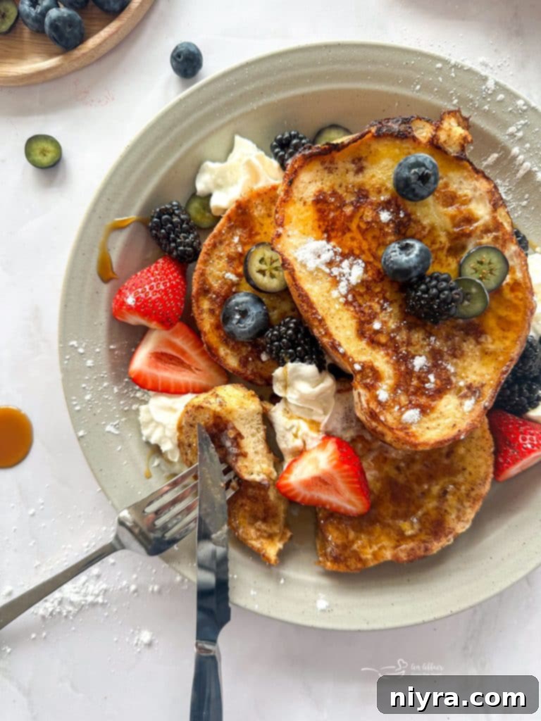 Golden-brown French toast slices with fresh berries and powdered sugar on a plate.