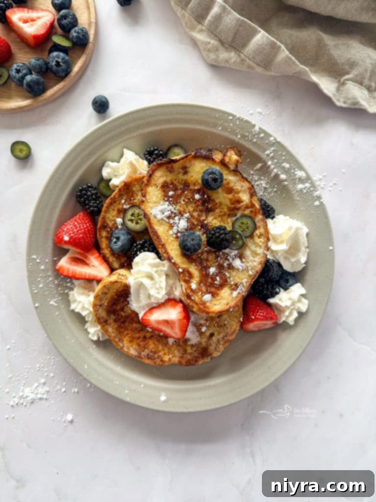 Cooked French toast slices topped with powdered sugar, fresh berries, and whipped cream.