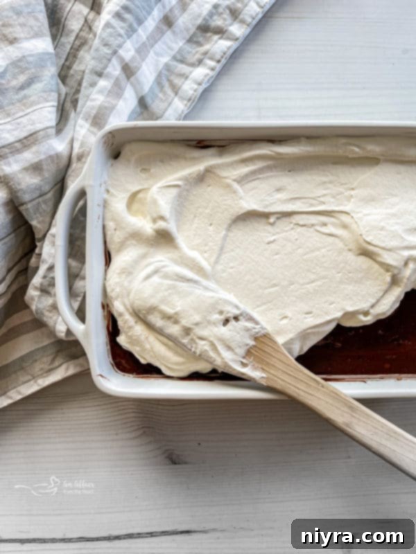 Spreading whipped cream over the cooled chocolate pudding poke cake