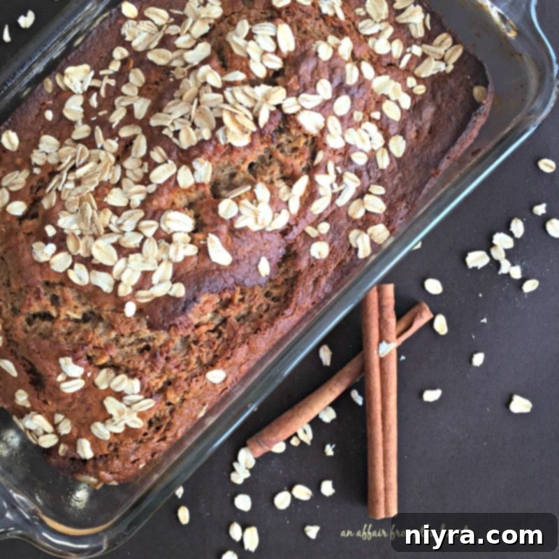 A golden-brown loaf of Banana Applesauce Oatmeal Bread, sliced and ready to serve, sitting on a wooden cutting board.
