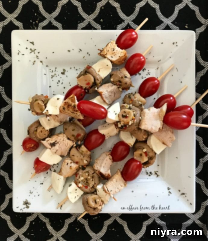 A cluster of grilled chicken, mozzarella, grape tomato, and marinated mushroom skewers on a white background, highlighting their fresh appeal.