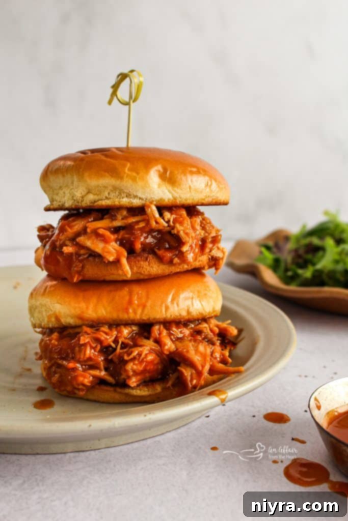 Close-up of Dr. Pepper BBQ Pork Sandwiches, piled high with shredded pork and sauce on a bun.