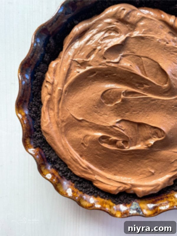 Top view of a chocolate pie filling, covered with plastic wrap, chilling in a pie dish.