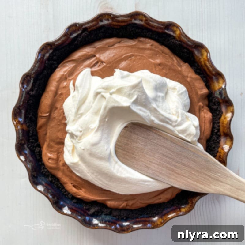 Freshly whipped topping being spread onto a chilled chocolate pie filling, creating a beautiful contrast.